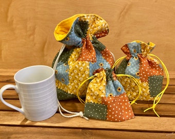 May include: Three fabric drawstring bags in various sizes, with a patchwork design of yellow, blue, green, and orange squares. The bags are made of cotton fabric and have a yellow drawstring.