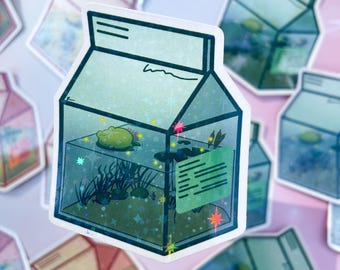 May include: A sticker featuring a milk carton design with a whimsical aquatic scene. Inside the carton, a yellow frog floats among aquatic plants and sparkling details. The carton has a light blue and green color scheme with a holographic effect.