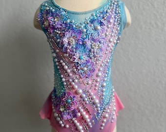 May include: A sleeveless leotard featuring a gradient of blue to pink fabric. The garment is heavily embellished with purple and blue floral lace appliqués, numerous white pearls of varying sizes, and clear crystals arranged in intricate patterns.