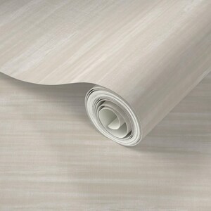 May include: A roll of neutral-toned wallpaper with a subtle, textured pattern. The paper is a light beige color with horizontal streaks, creating a soft, artistic effect. The roll is partially unrolled, revealing the inner white core.
