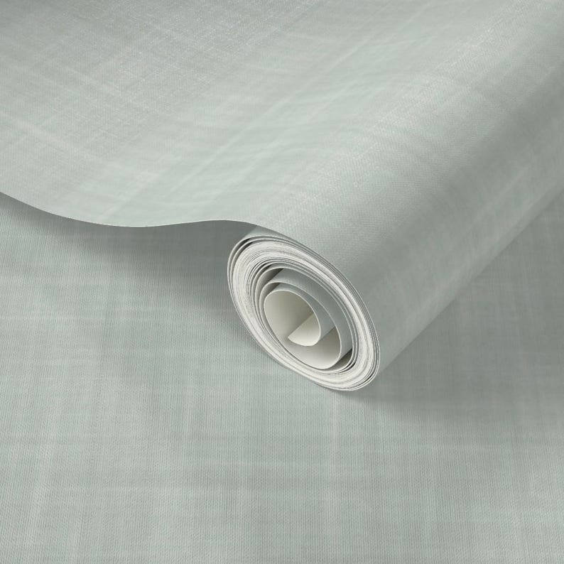 K&ouml;nnte beinhalten: Eine Rolle hellblaues Tapetenmaterial mit einem dezent strukturierten Muster. Die Tapete ist teilweise abgerollt und zeigt die wei&szlig;e R&uuml;ckseite. Das Design wirkt weich und dezent, passend f&uuml;r verschiedene Einrichtungsstile.