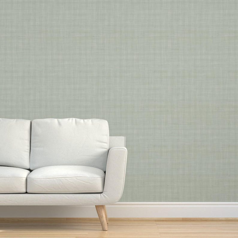 K&ouml;nnte beinhalten: Ein wei&szlig;es Sofa mit Holzbeinen steht vor einer hellgr&uuml;nen, strukturierten Wand. Das Sofa hat ein minimalistisches Design mit einer klaren, modernen &Auml;sthetik. Die Wand hat ein subtiles, gewebtes Muster.