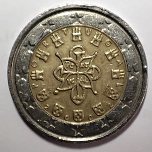May include: A silver and gold 2 Euro coin from Portugal. The coin features a stylised image of a coat of arms with the inscription "PORTUGAL" around the edge.