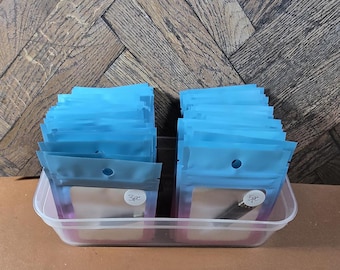 May include: A clear plastic container filled with small blue resealable bags. The bags are labeled with the text "3pc" and "5pc".