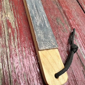 May include: A wooden sharpening tool with a grey sanding surface and a black cord attached. The tool is sitting on a red wooden surface.