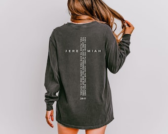 May include: A charcoal gray long-sleeve shirt featuring a white graphic on the back. The design includes a vertical cross shape formed by the text Jeremiah 29:11, which reads: For I know the plans I have for you, declares the Lord, plans to prosper you and not to harm you, plans to give you a hope and a future.