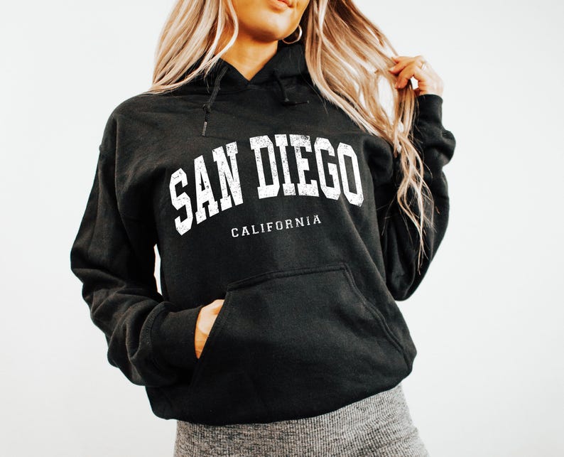 May include: Black hooded sweatshirt with the text "SAN DIEGO CALIFORNIA" in white block letters. The sweatshirt has a front pocket and a drawstring hood. The garment is made of a soft, comfortable material.