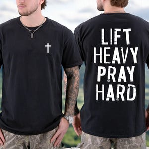 May include: Black t-shirt with a white cross on the front and the words "LIFT HEAVY PRAY HARD" on the back. The shirt is a crew neck and has short sleeves. The shirt is made of a soft material.