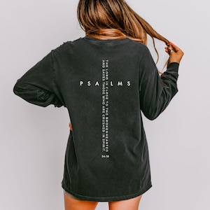 May include: Dark gray long-sleeve shirt with the text "PSA LMS" in white, arranged in a cross shape. The shirt also features the quote "THE LORD IS CLOSE TO THE BROKENHEARTED AND SAVES THOSE WHO ARE CRUSHED IN SPIRIT. 34:18" in white.
