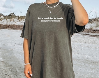 May include: Olive green t-shirt with the text "it's a good day to teach computer science" in white. The shirt has short sleeves and a relaxed fit. The shirt is made of a soft material.