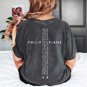 May include: Dark gray t-shirt with the word "PHILIPPIANS" and the text "WHATEVER IS TRUE..." printed in white. The shirt has short sleeves and a relaxed fit. The text includes the verse "4:8".