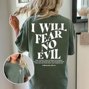 May include: An olive green t-shirt with the text "I WILL FEAR NO EVIL" in large white letters on the back. A Bible verse is printed below the text. A small image shows a white cross on the front of the shirt.