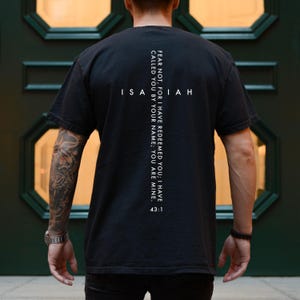May include: Black t-shirt with white text. The text includes the word "Isaiah" in a cross shape, and the quote "FEAR NOT, FOR I HAVE REDEEMED YOU; I HAVE CALLED YOU BY YOUR NAME; YOU ARE MINE. 43:1".