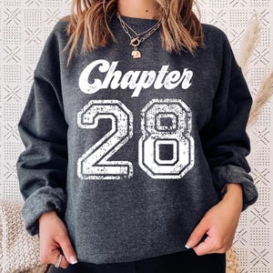 May include: Dark gray sweatshirt with the text "Chapter 28" in distressed white lettering. The number 28 is in a collegiate font. The sweatshirt has long sleeves and a crew neck.