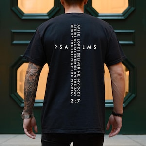 May include: Black t-shirt with white text on the back. The text includes the words "ARISE, LORD! DELIVER ME, MY GOD! STRIKE ALL MY ENEMIES ON THE JAW; BREAK THE TEETH OF THE WICKED." and "PSA LMS 3:7".