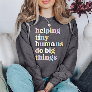 May include: A dark grey sweatshirt with the text "helping tiny humans do big things" in rainbow colours.
