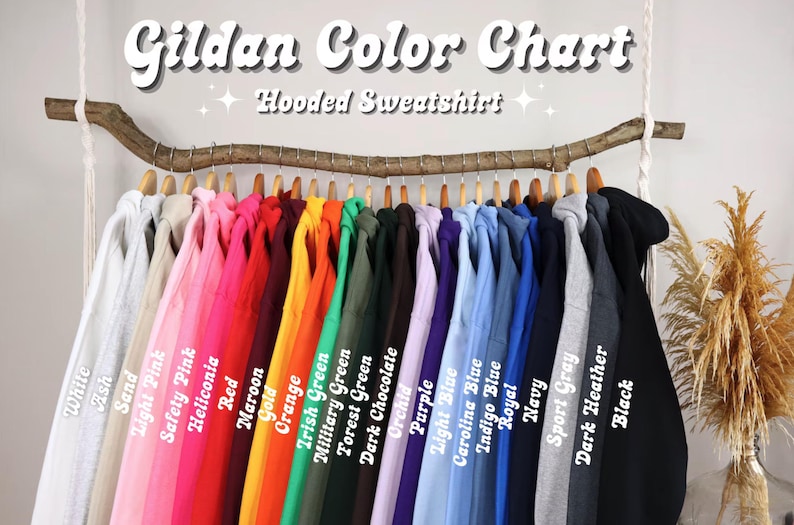 May include: A color chart for Gildan hooded sweatshirts, displaying a variety of colors including white, pink, red, orange, green, blue, gray, and black. The sweatshirts are hanging on a wooden rod, with the color names labeled below each garment.