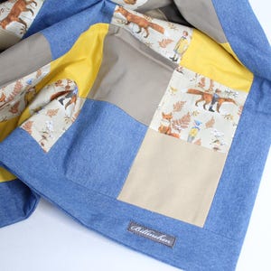 Könnte beinhalten: Eine Patchwork-Decke mit einem blauen Jeansrand. Die Decke besteht aus verschiedenen Stoffen mit einem Fuchs- und Waldtierdruck. Die Decke hat ein gelbes, beiges und weißes Farbschema. Die Decke hat ein Etikett mit der Aufschrift "Ballerina".