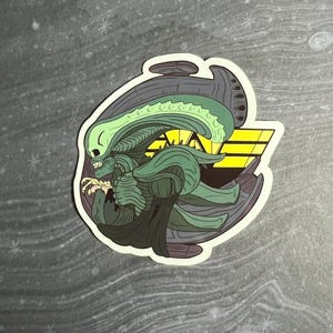 May include: A sticker featuring a stylized illustration of an alien creature in shades of green, gray, and yellow. The design includes a detailed head, body, and a geometric background. The sticker has a white border.