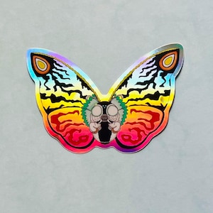 May include: A holographic sticker of a colorful butterfly with a black and yellow striped pattern. The butterfly has a red and orange body with a green head and two white eyes.