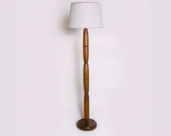 Könnte beinhalten: Eine Stehlampe mit einem weißen Stoffschirm und einem zylindrischen Holzfuß.