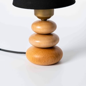 May include: A black lampshade sits atop a stack of three wooden, round, light brown lamp bases.