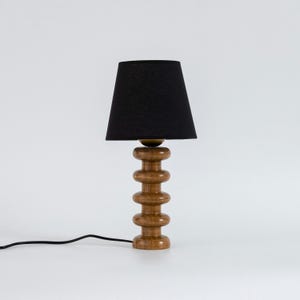 May include: A wooden table lamp with a black fabric lampshade. The lamp base is made of stacked wooden rings.