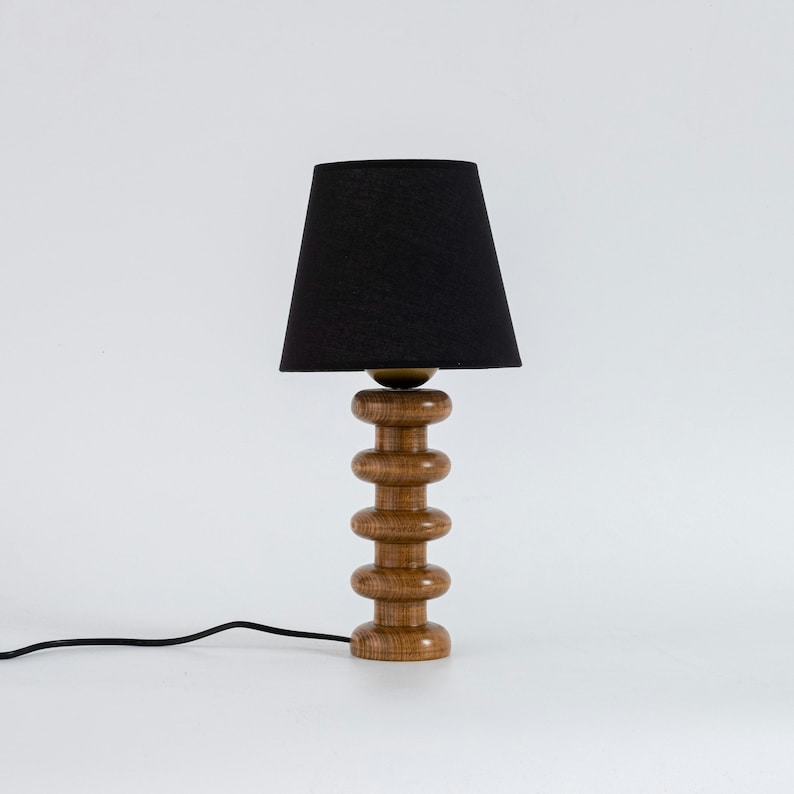 May include: A wooden table lamp with a black fabric lampshade. The lamp base is made of stacked wooden rings.