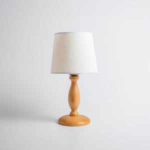 May include: A wooden table lamp with a white linen lampshade. The lamp has a simple, elegant design and would be a great addition to any home.