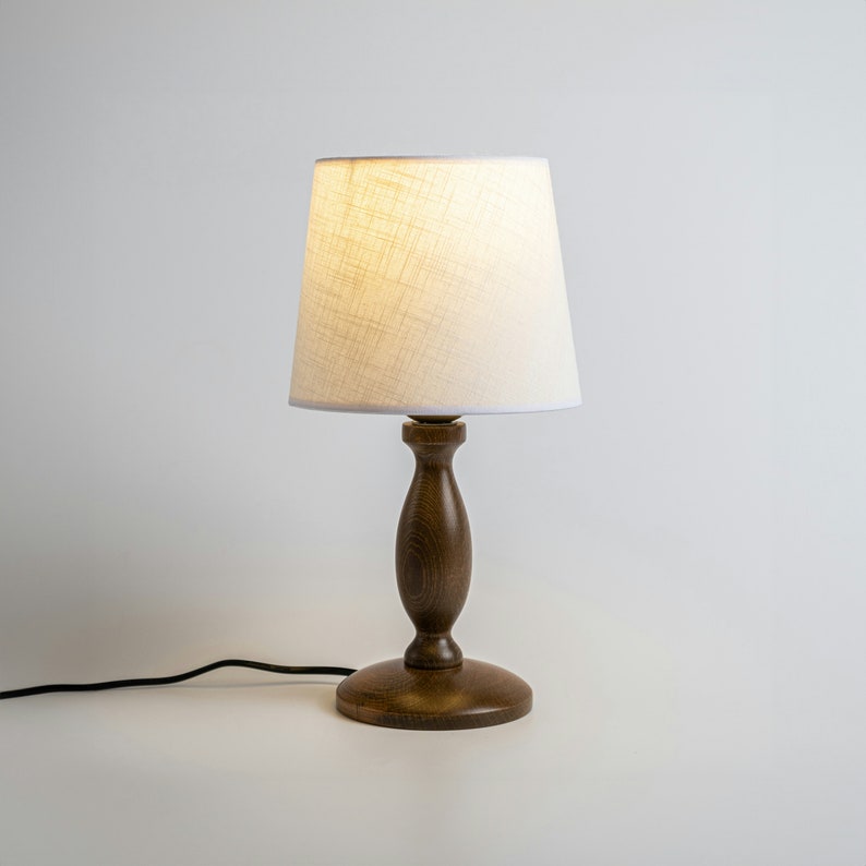 May include: A wooden table lamp with a white linen shade. The lamp has a dark brown finish and a simple design.