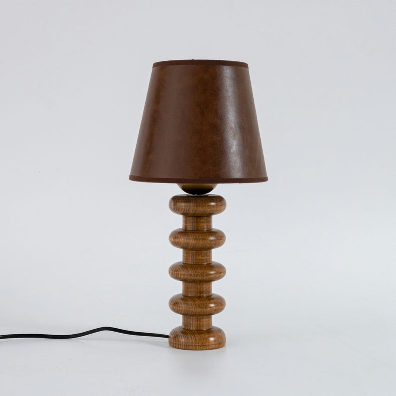 May include: A wooden table lamp with a brown fabric lampshade. The lamp base is made of stacked wooden rings.