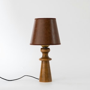 May include: A wooden table lamp with a brown leather lampshade. The lamp has a round base and a tall, slender stem.