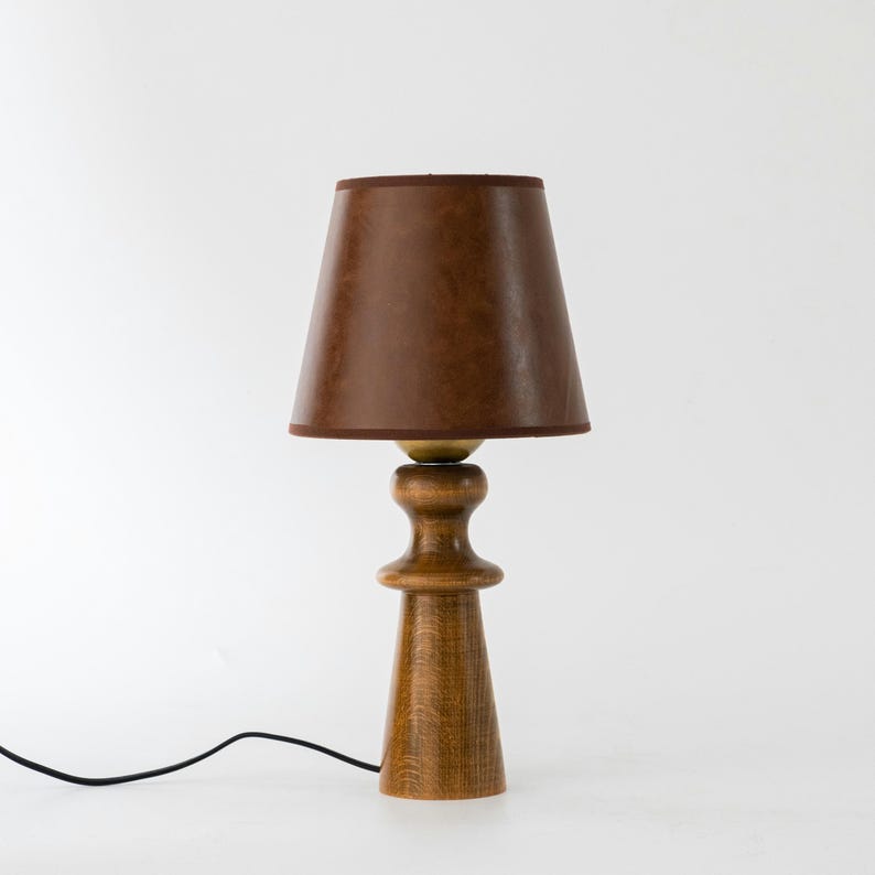 May include: A wooden table lamp with a brown leather lampshade. The lamp has a round base and a tall, slender stem.