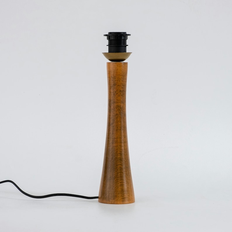 May include: A wooden table lamp with a brown finish and a black cord. The lamp has a simple design with a round base and a tall, slender stem.