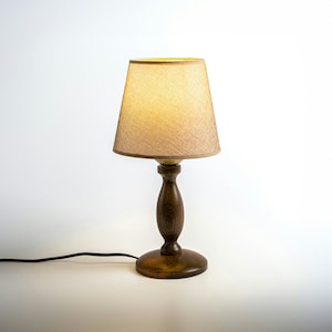 May include: A wooden table lamp with a beige fabric lampshade. The lamp has a dark brown wooden base and a cord.