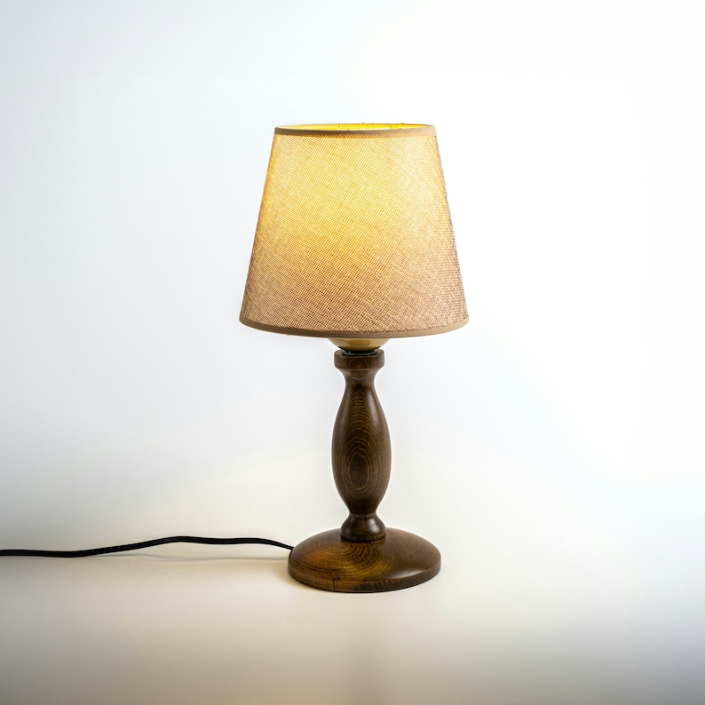 May include: A wooden table lamp with a beige fabric lampshade. The lamp has a dark brown wooden base and a cord.
