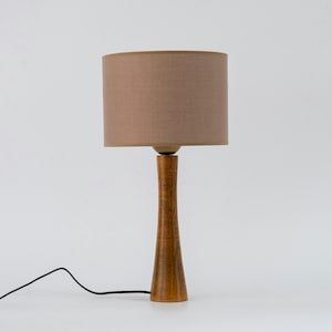 May include: A wooden table lamp with a brown linen lampshade. The lamp has a tall, slender base and a simple design.