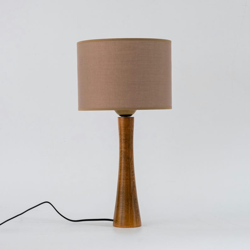 May include: A wooden table lamp with a brown linen lampshade. The lamp has a tall, slender base and a simple design.