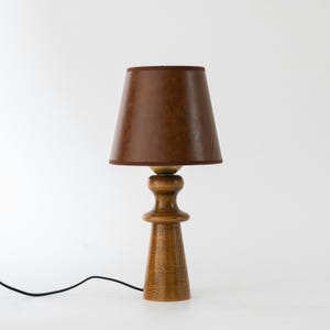 May include: A wooden table lamp with a brown leather lampshade. The lamp has a round base and a tall, slender stem.