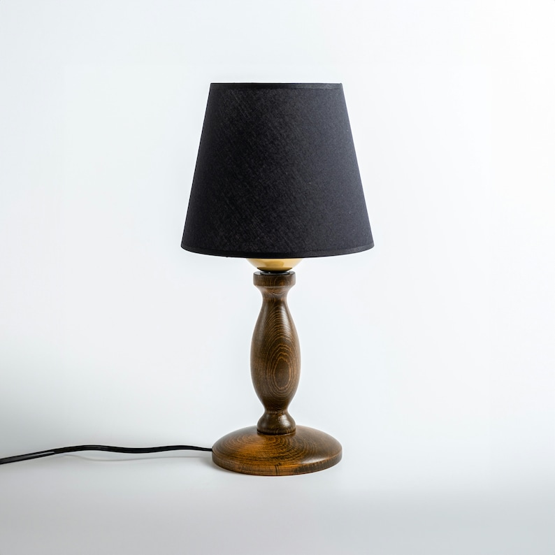 May include: A wooden table lamp with a black fabric lampshade. The lamp has a dark brown wooden base with a gold-colored accent.