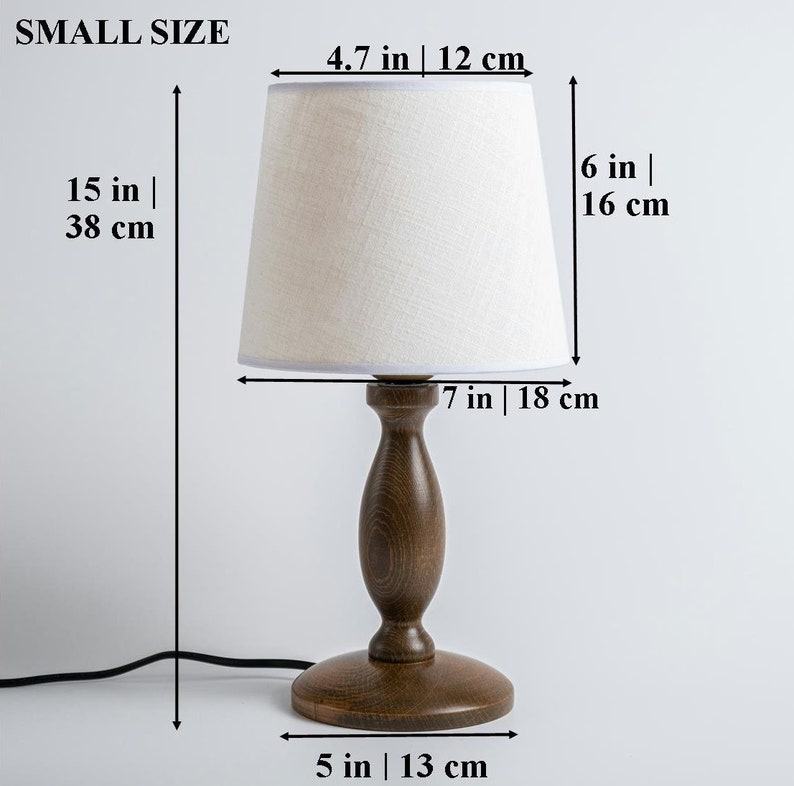 May include: A small, wooden table lamp with a white linen lampshade. The lamp is 15 inches tall and the shade is 6 inches tall. The base of the lamp is 5 inches in diameter.