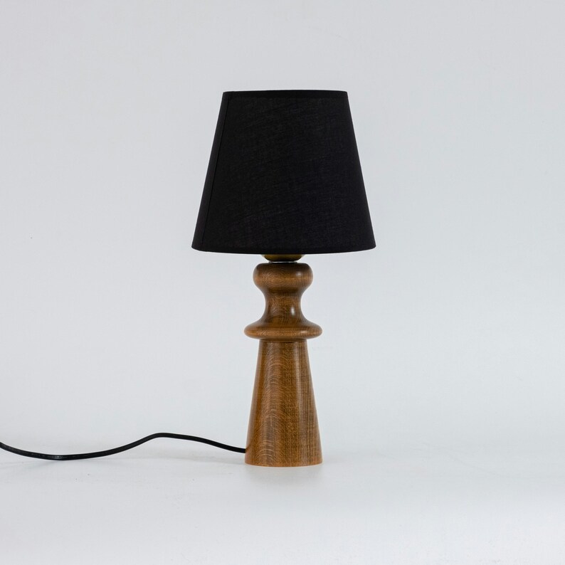 May include: A wooden table lamp with a black fabric lampshade. The lamp has a simple, modern design and is perfect for adding a touch of style to any room.