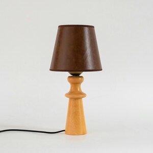 May include: A wooden table lamp with a brown fabric lampshade. The lamp has a simple, mid-century modern design.