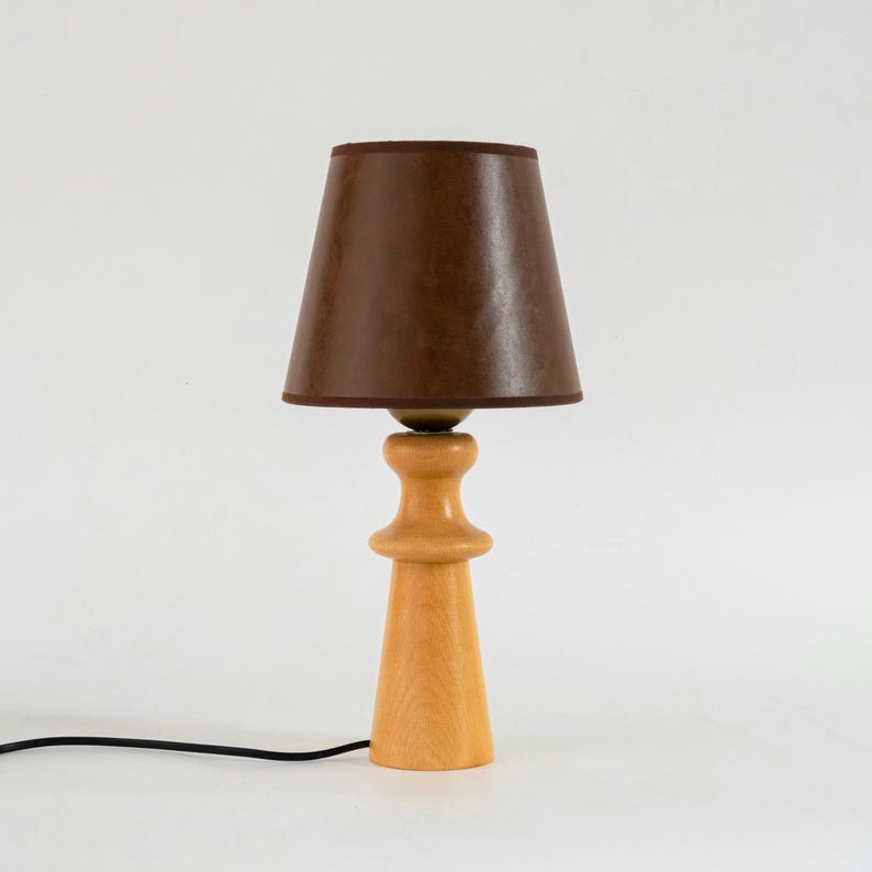 May include: A wooden table lamp with a brown fabric lampshade. The lamp has a simple, mid-century modern design.