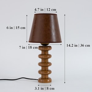 May include: A wooden table lamp with a brown leather lampshade. The lamp is 14.2 inches tall and has a 6-inch diameter base. The lampshade is 4.7 inches in diameter.