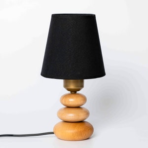 May include: A black lampshade with a wooden base that resembles stacked stones. The base is made of three rounded pieces of wood.