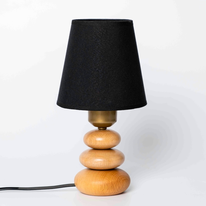 May include: A black lampshade with a wooden base that resembles stacked stones. The base is made of three rounded pieces of wood.