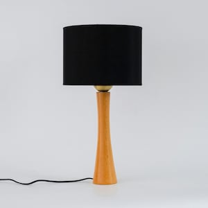 May include: A wooden table lamp with a black fabric shade. The lamp has a tall, slender base and a simple design.