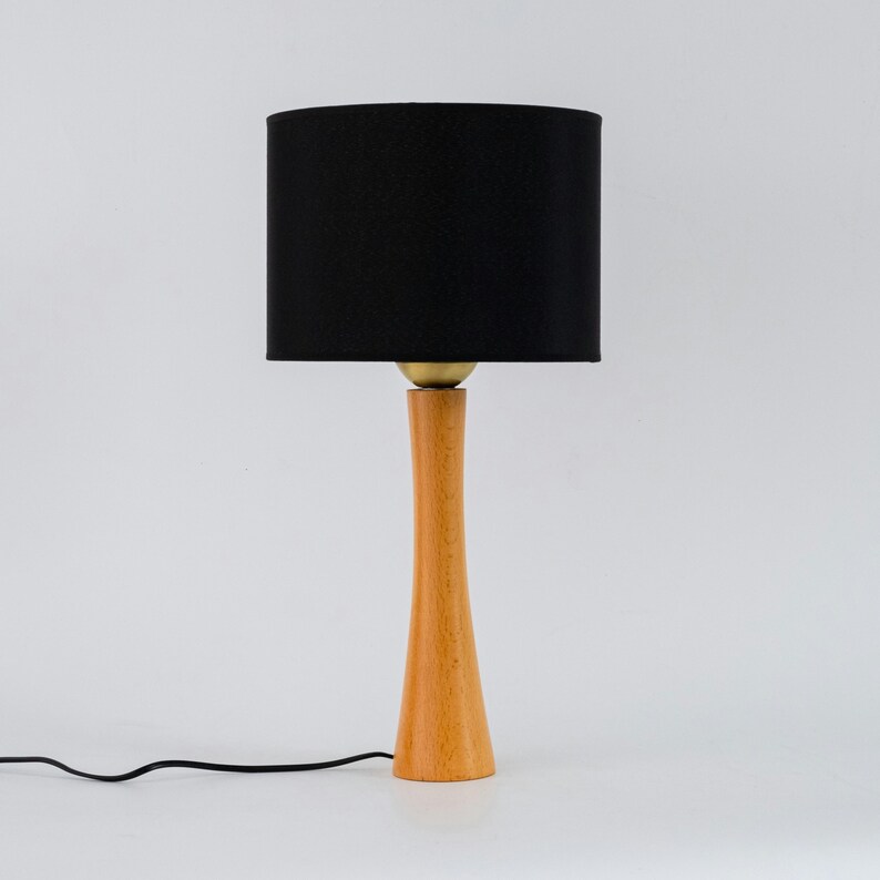 May include: A wooden table lamp with a black fabric shade. The lamp has a tall, slender base and a simple design.