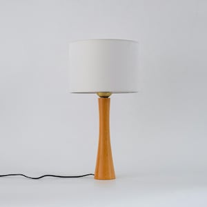 May include: A wooden table lamp with a white fabric shade. The lamp has a slender, tapered base.